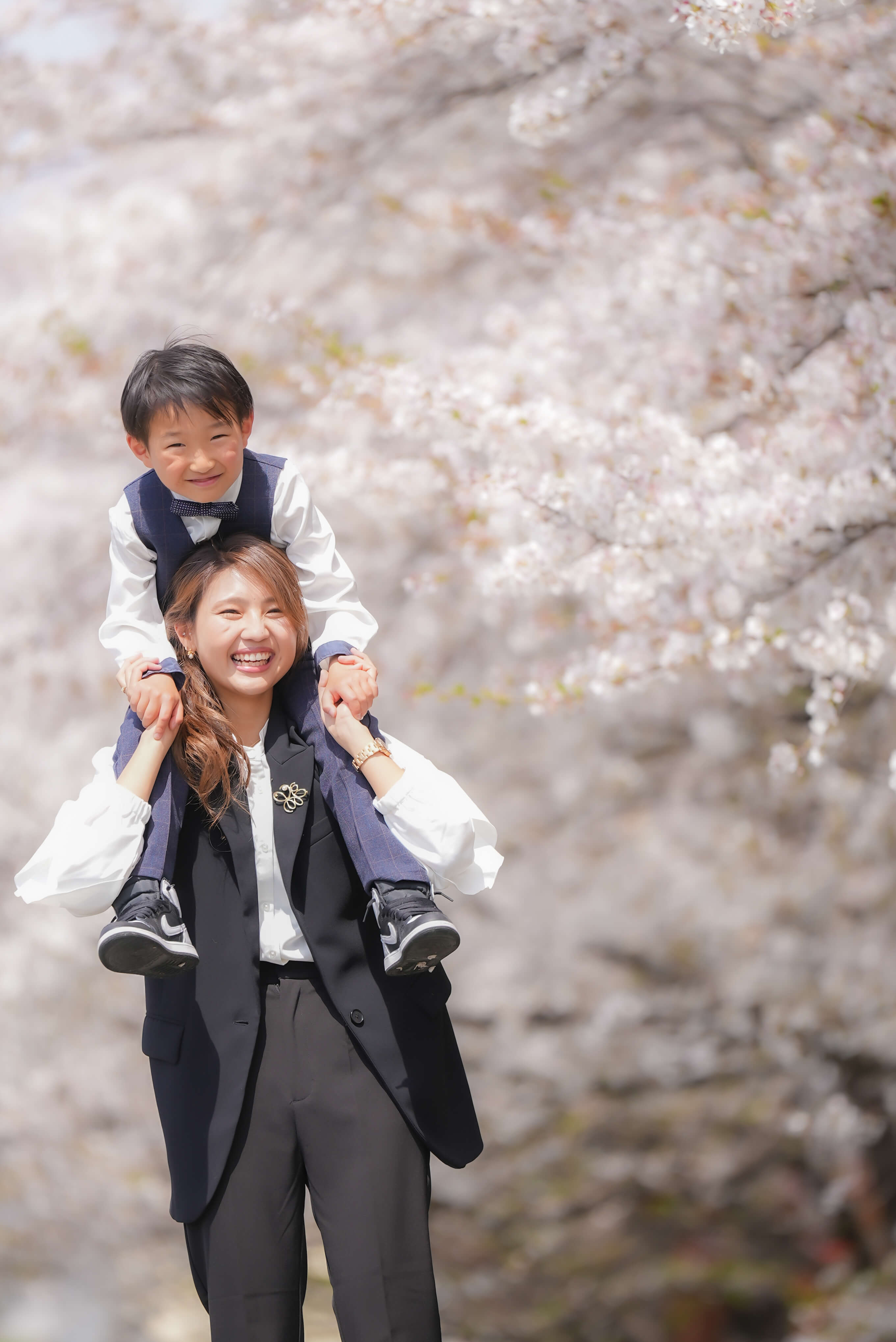 満開の桜の下、母の肩に乗る男の子を写したFlog Filmの家族写真