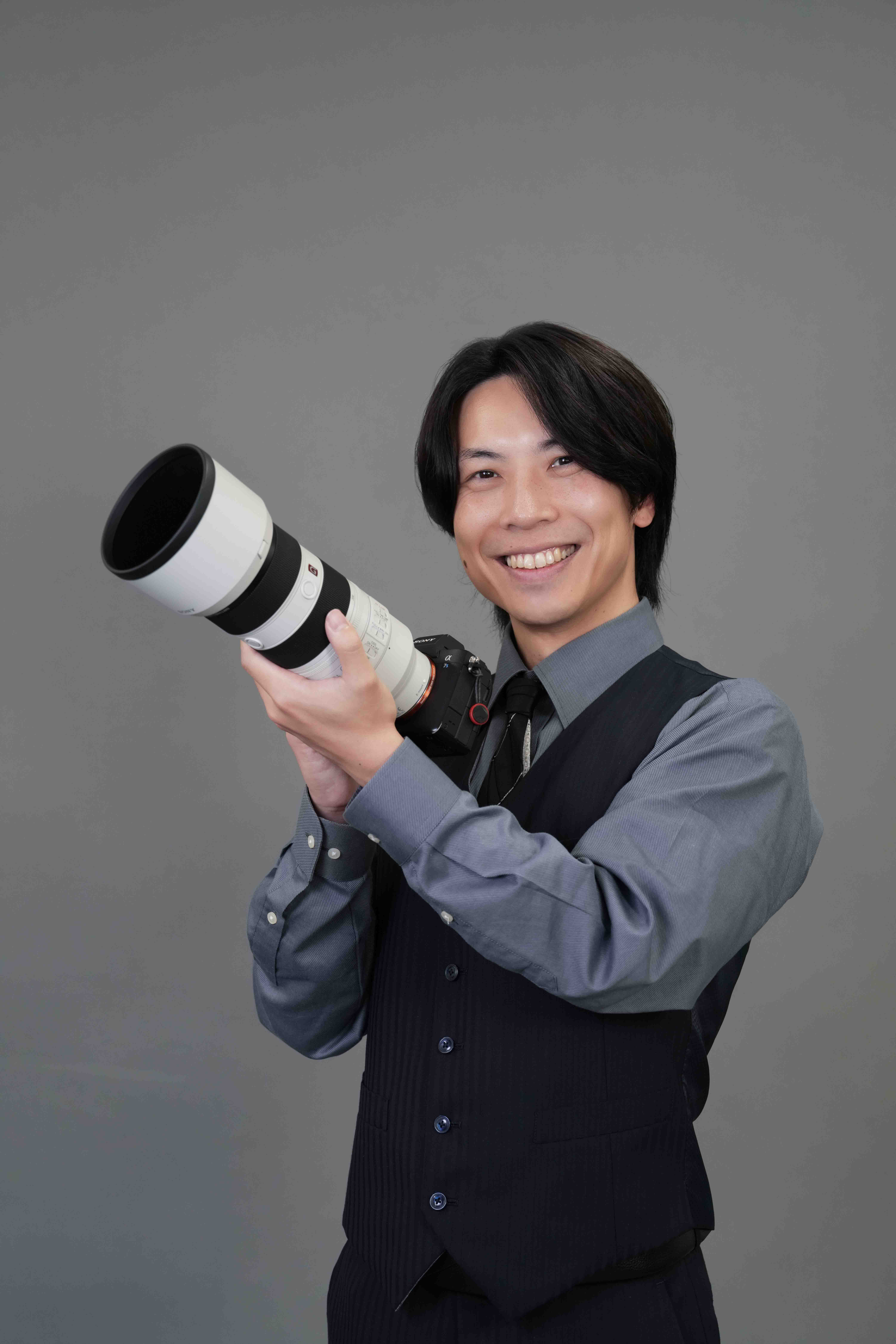 望遠レンズのカメラを構えて微笑むFlog Film代表の写真